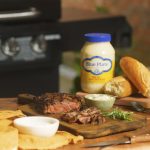 Grilled steak sliced on serving board with jar of Blue Plate Mayo in background