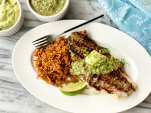 Individual portion of Grilled Red Snapper with Avocado Mayonnaise and Salsa Verde served on a plate with lime wedge