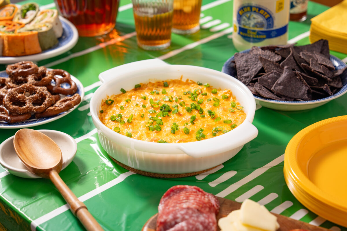 Bayou Hot Chicken Dip in a serving bowl with other game day food. Made with Blue Plate - That's the good stuff.
