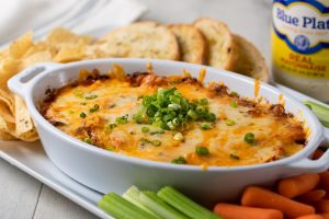 Bayou Hot Chicken Dip in a baking dish with crackers and cut vegetables on the side