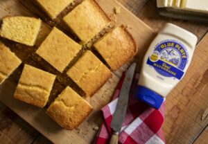 easy cornbread made with blue plate mayonnaise, cut into squares on a wooden cutting board, with butter