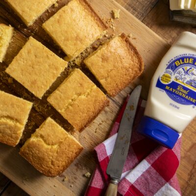easy cornbread made with blue plate mayonnaise, cut into squares on a wooden cutting board, with butter